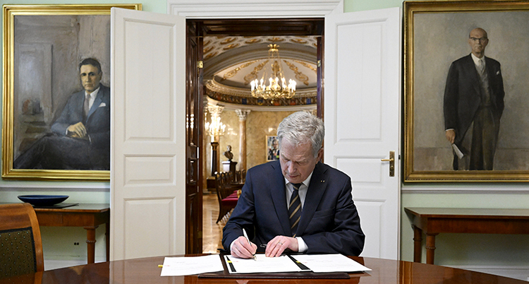 Presidenten skriver på ett papper som ligger på ett stort bord.