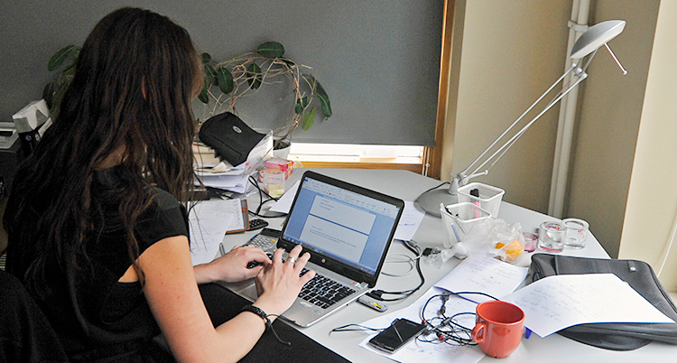 En kvinna sitter vid ett skrivbord och skriver på en dator. Vi ser henne bakifrån.