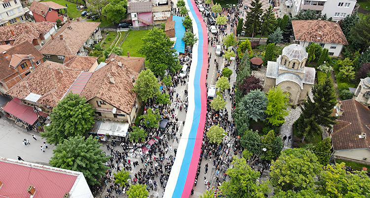 En bild från luften som visar hur människor håller en lång flagga längs en gata.