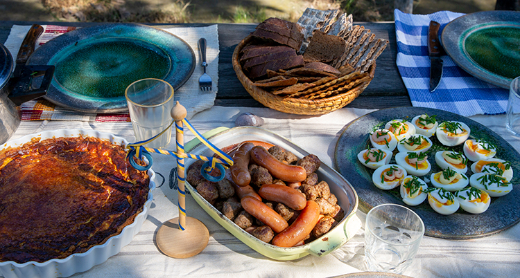 Ett bord utomhus dukat med tallrikar och olika mat med mat och bröd.