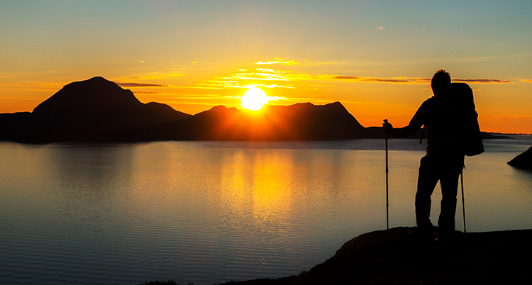 En man framför en sol som ser tu att gå ner över havet.