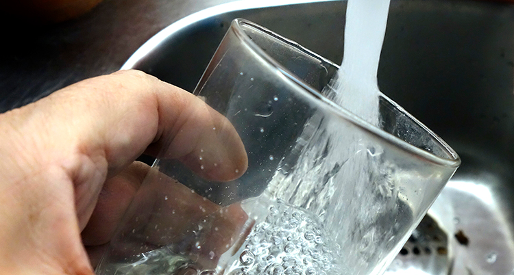 En hand håller ett glas under en vattenkran