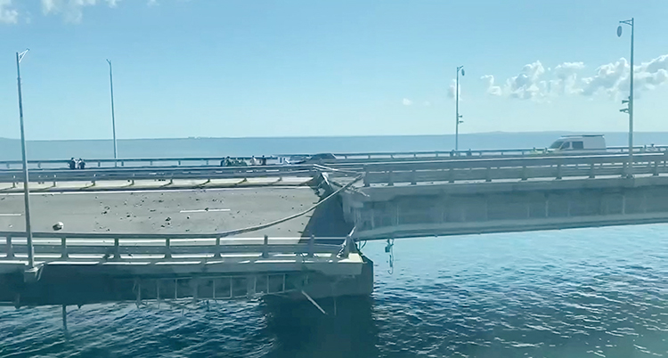 En bro går över vattnet. En del av bron är trasig och hänger ner.