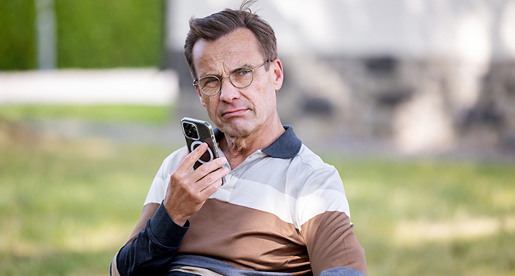 Ulf Kristersson sitter utomhus och håller i en mobiltelefon.