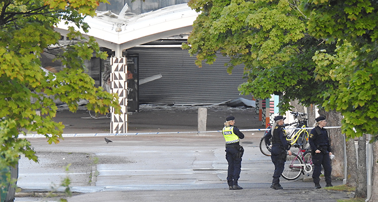 Tre poliser står på ett torg utanför en restaurang som blivit skadad.