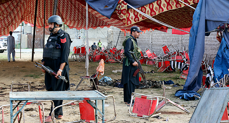 Två poliser står och vaktar vid ett stort tält. Tältet och massor av stolar är skadade efter en explosion.