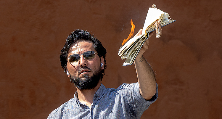 En man i halvfigur håller upp en brinnande bok.
