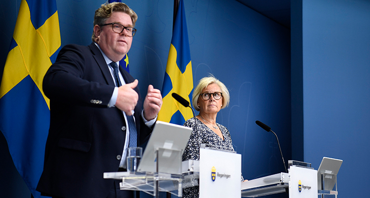 De står bredvid varandra bakom varsin talarstol. Det är svenska flaggor bakom.