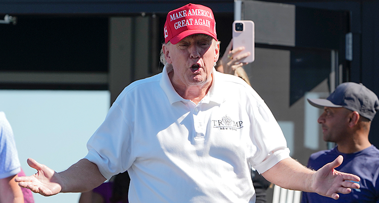 Donald Trump står och pratar med en vit skjorta och röd keps.