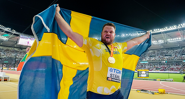 Han går runt på en arena. Han är glad. Han lyfter upp en stor svensk flagga.
