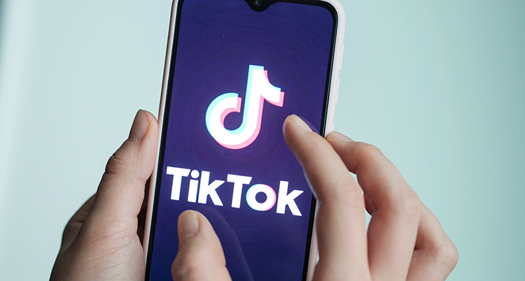 Två händer håller i en mobil där appen Tiktok syns på skärmen.