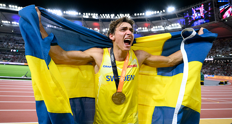 Han håller upp en svensk flagga och jublar med guldmedalj runt halsen. och flagga