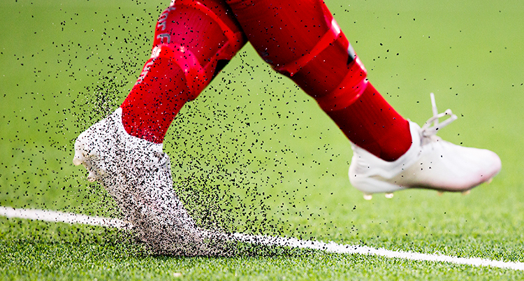 En närbild på ett par ben i en fotbollsmatch. Små kulor av plast flyger i luften när benen rör sig.
