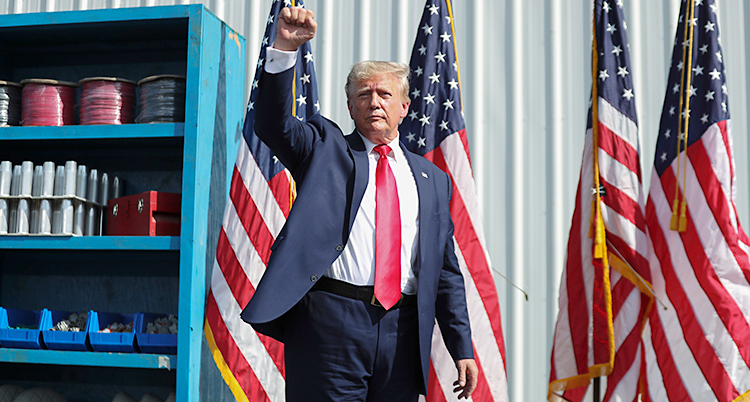 Han står på en scen. Han håller upp sin knutna näve. I bakgrunden syns flera amerikanska flaggor.