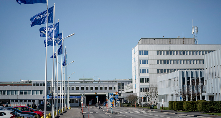 Fabriken i Göteborg. Flaggor och en bilparkering syns.