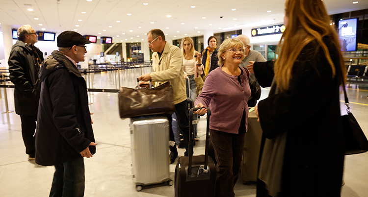Hon sträcker armarna mot en kvinna. Bakom syns flera personer med väskor. De är på en flygplats.