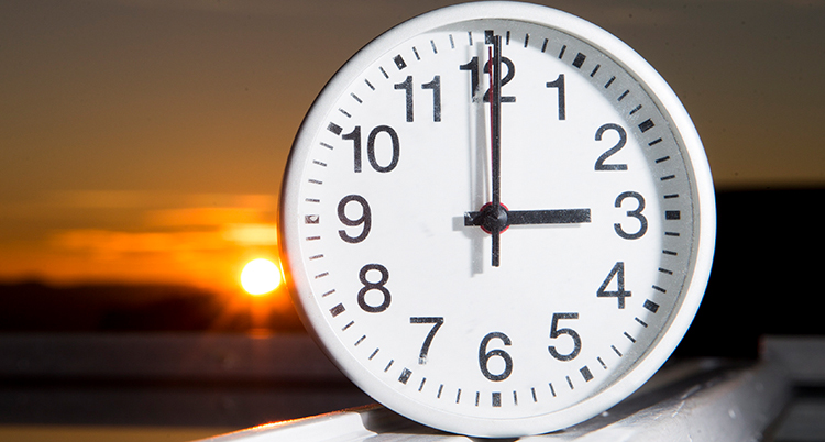 En klockan som visar klockan tre. Solnedgång i bakgrunden.