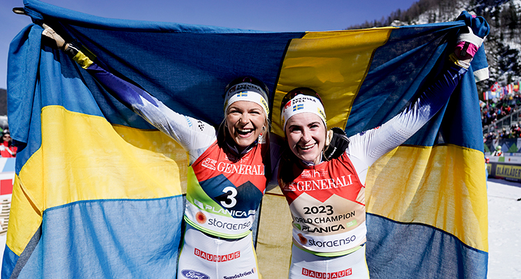 De håller upp en stor svensk flagga bakom sig och är glada.
