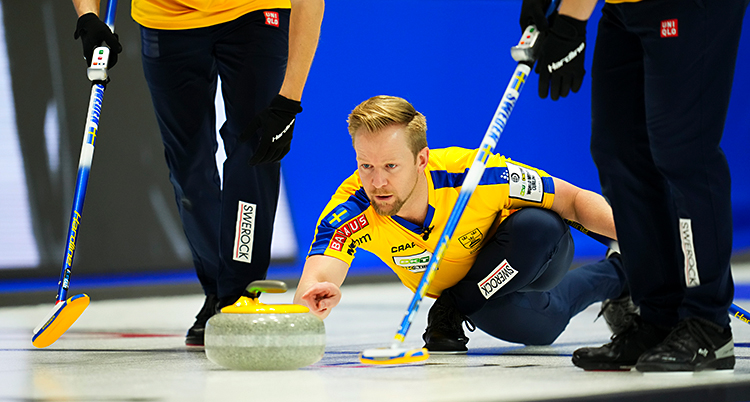 Från en match i curling. Niklas Edin skickar iväg en sten på isen. Två andra i laget gör sig beredda att sopa.