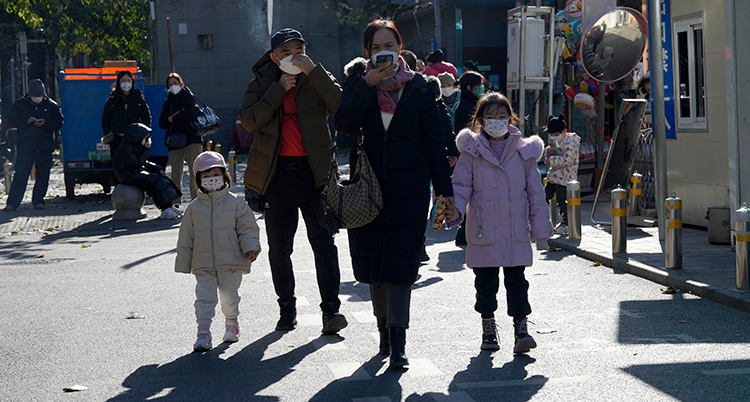 Två barn och två vuxna går på en gata. De har munskydd på sig.