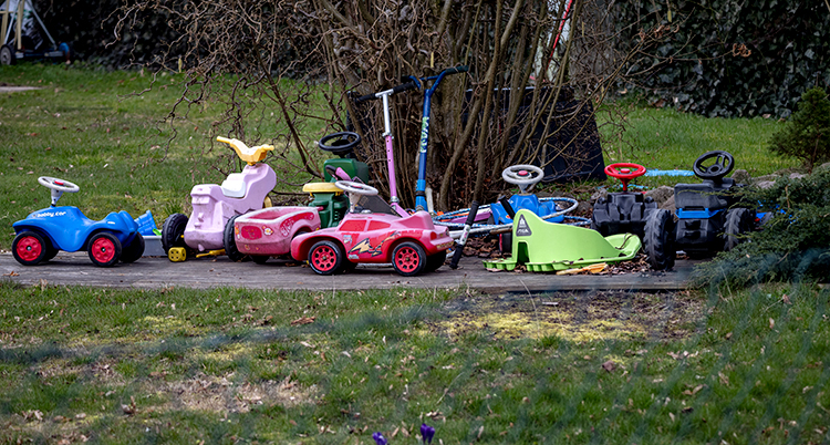 Bobbycar-bilar och andra leksaker står uppställda vid ett träd.
