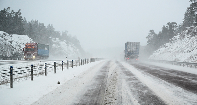 En väg med snö. Två lastbilar kör på vägen.