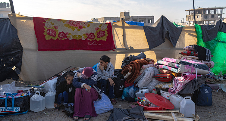 En kvinna och några barn sitter framför lite packning vid ett tältläger.