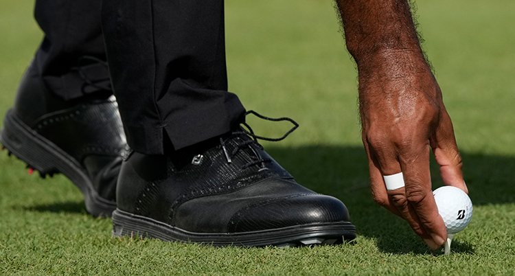 Bara fötter och en hand från en golfspelare syns. Han placerar en golfboll på en peg.