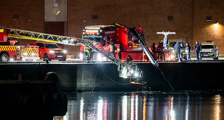 Det är mörkt ute. En brandbil står på kanten framför vattnet.