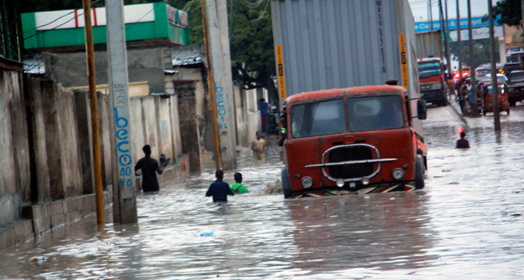 Människor står i vattnet på gatan i staden. Vattnet når utt till midjan på dem. En lastbil över översvämmad.