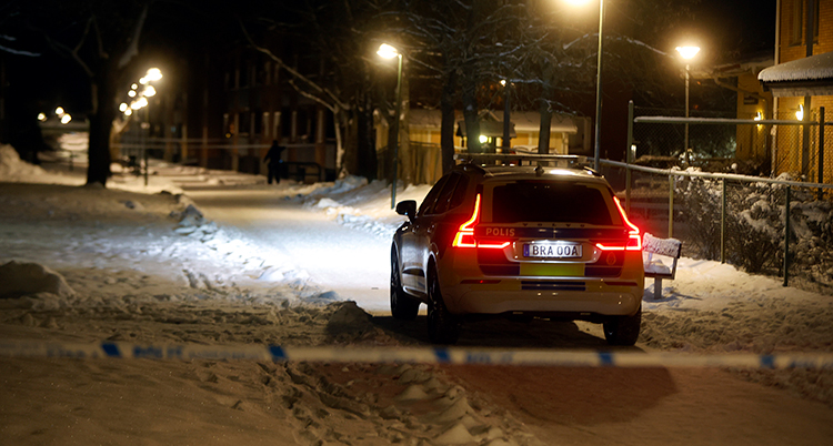 En polisbil framför ett avspärrningsband på en snöig gata.