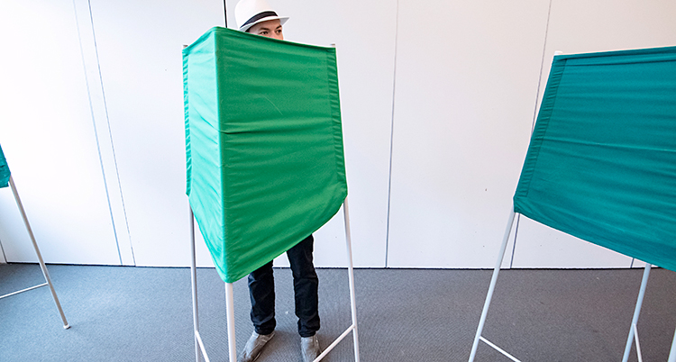 En man står i ett grönt bås i en vallokal.