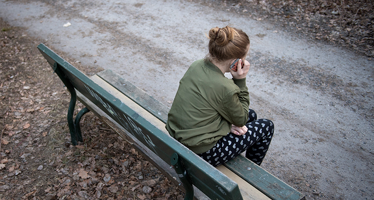 En flicka sitter på en bänk och pratar i en mobiltelefon.
