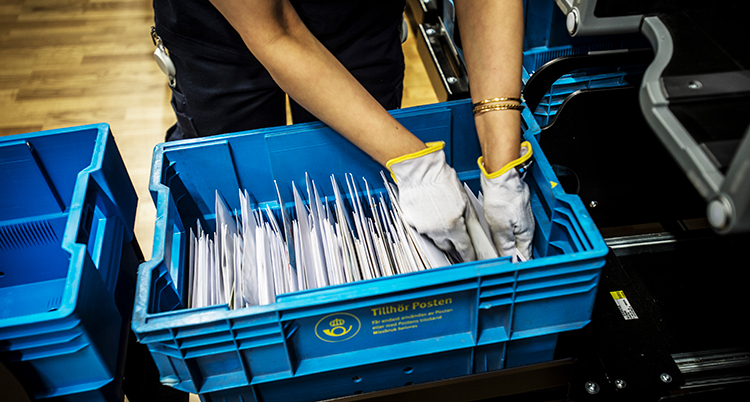 En person med plasthandskar sorterar brev som finns i en blå låda.