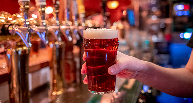 En hand håller i en öl vid en bar.