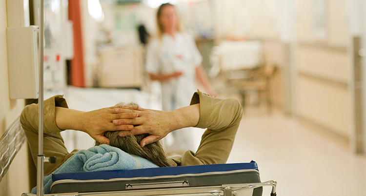 En patient ligger i en säng i en korridor på ett sjukhus.