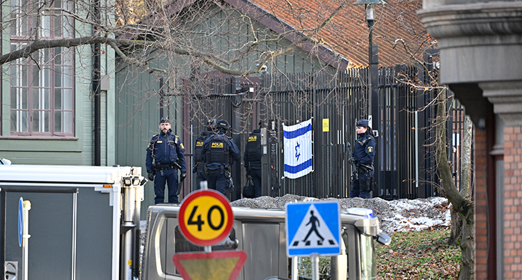 En bild på ett staket taget på långt håll. Poliser står vid staketet. Där hänger också Israels flagga.