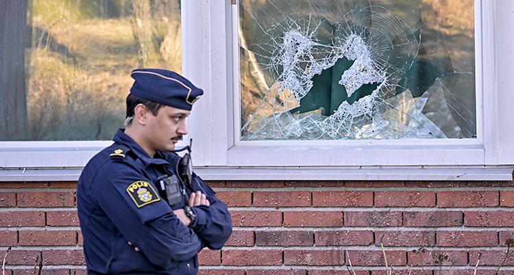 En polis står utanför ett hus där ett fönster är trasigt.