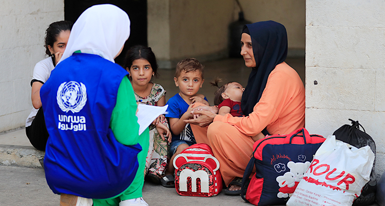 En kvinna från Unrwa sitter på huk och pratar med en kvinna som sitter med några barn.