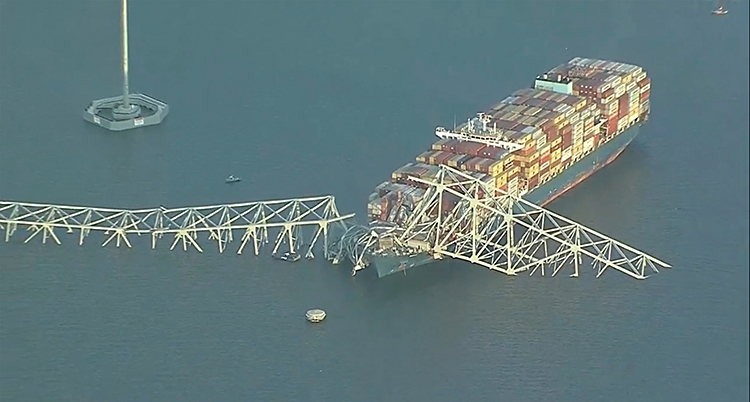 En bild från luften som visar en stor båt som är lastad med massor av containrar. Båten har kört in i en bro.