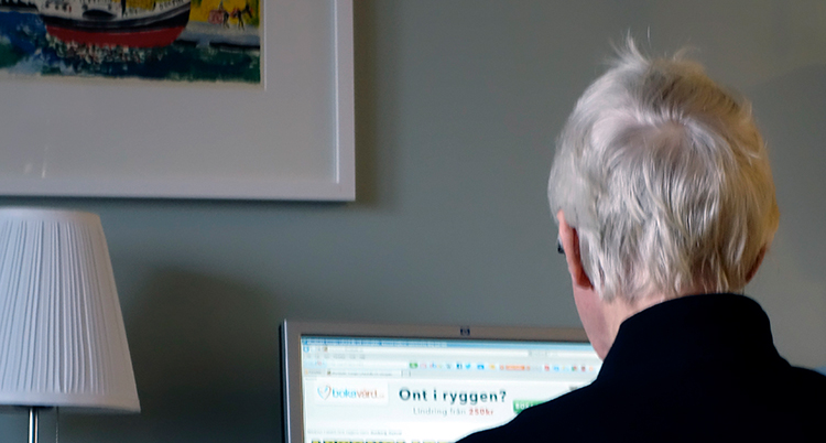 En man med grått hår sitter framför en datorskärm. Han syns bakifrån.