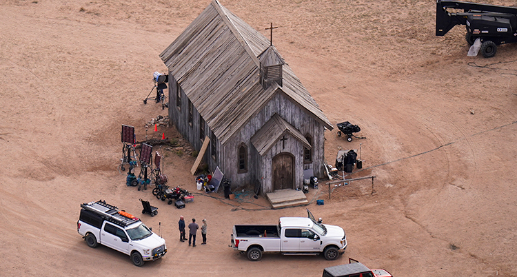 Ett foto taget ovanifrån på en träkyrka som står ensligt på sandig mark. Runt kyrkan står personer och polisbilar.
