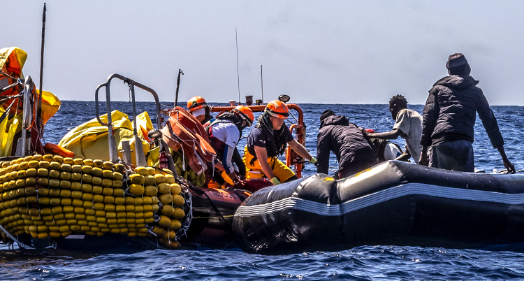 Folk från en räddningsbåt hjälper flera personer att lämna en gummibåt.