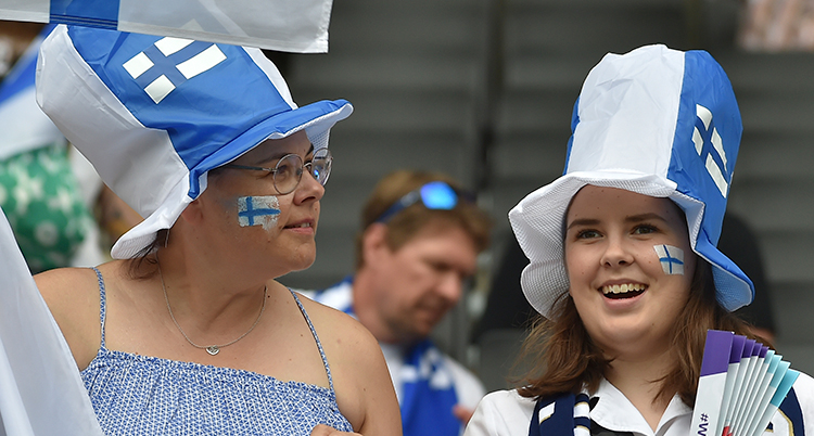 Två unga kvinnor med vitblå hattar och finska flaggor målade på kinderna.