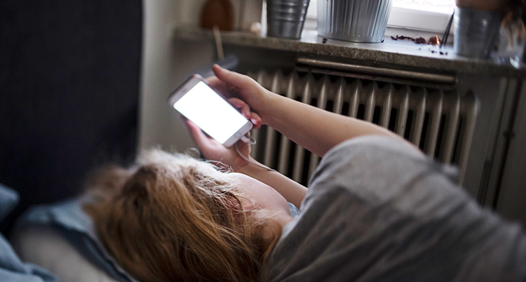 En kvinna ligger i en säng och håller i sin mobil.