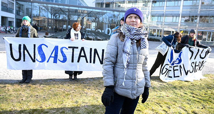 Hon står framför en banderoll med text som flera andra personer håller upp.