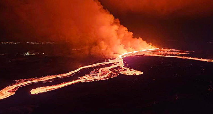 Långa strömmar med rödvit lava rinner på marken. Det är mörkt ute.