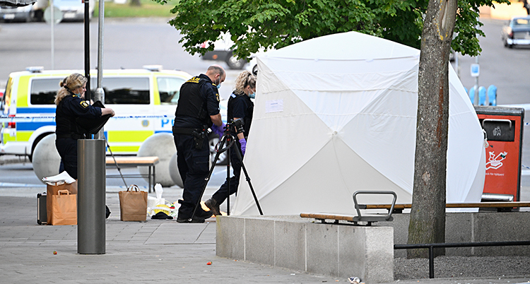 Tre poliser står och jobbar vid ett uppspänt vitt tält.