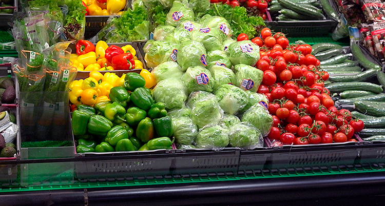 Paprikor och tomater och andra grönsaker i en grönsaksdisk i en affär.
