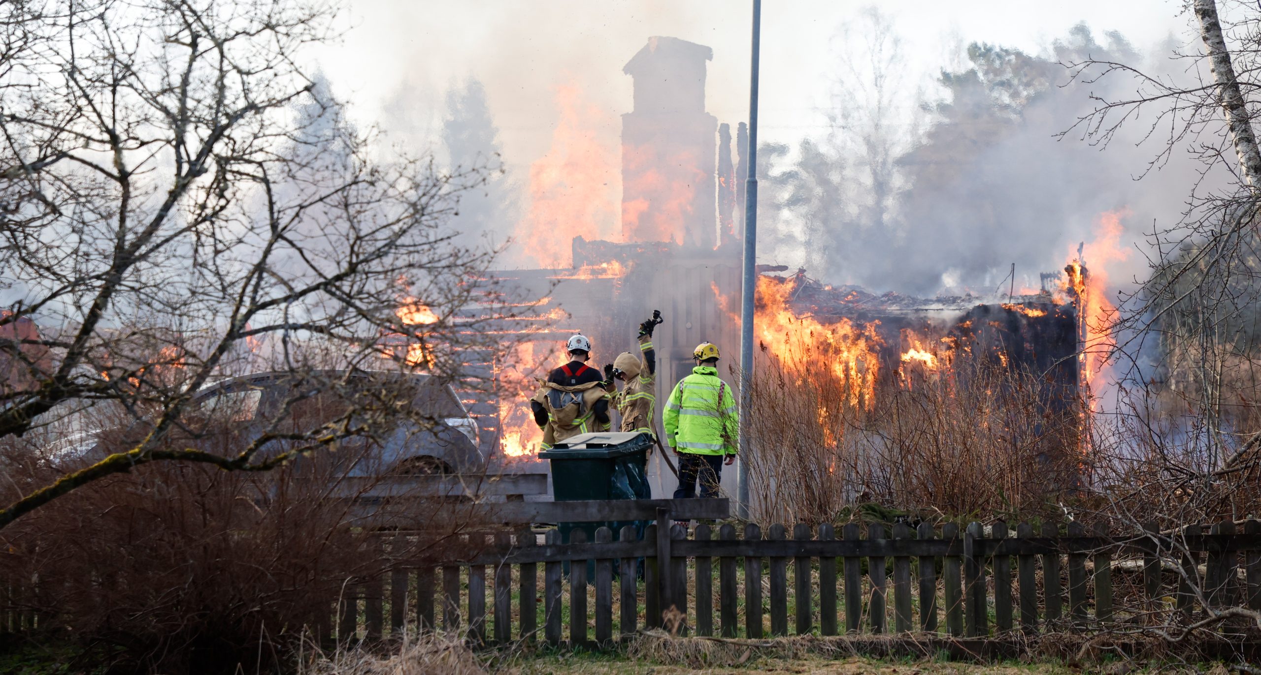 Brandmän står framför huset som brinner.